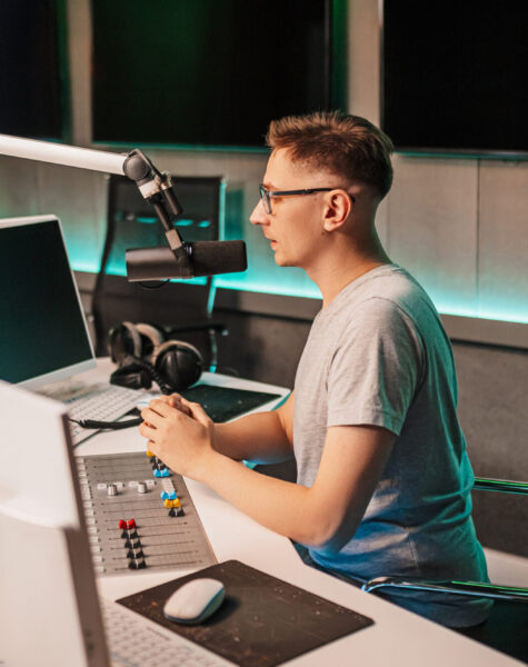 The DJ hosts the program and communicates with the audience on air at the radio station. The announcer reads the news. A male radio host speaks into a microphone and records a podcast