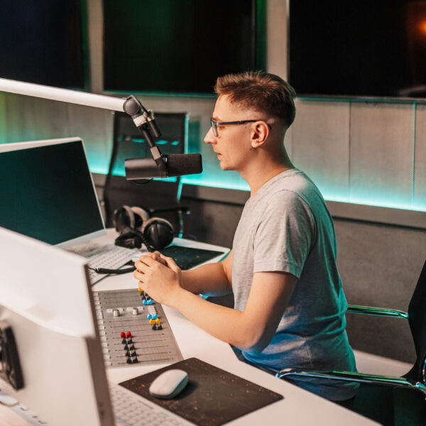 The DJ hosts the program and communicates with the audience on air at the radio station. The announcer reads the news. A male radio host speaks into a microphone and records a podcast