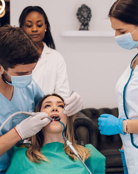 Attractive young woman in stomatology clinic being examined by a male dentist. Healthy teeth concept. Oral hygiene and dental care. Doctor fixing patient teeth with a help of a two assistant.